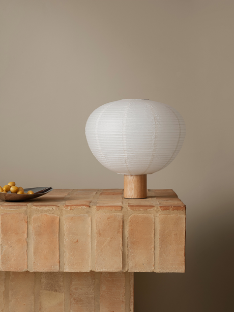 Moderne Tischlampe aus Papier und Holz auf einem Ziegelstein-Sockel vor neutralem Hintergrund.