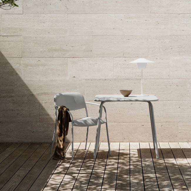 Moderne Möbel mit Tisch, Stuhl und Lampe auf einem Holzdeck mit sandfarbenen Wänden.