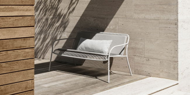 Moderne Gartenbank aus Metall vor einer Steinwand auf Holzterrasse.