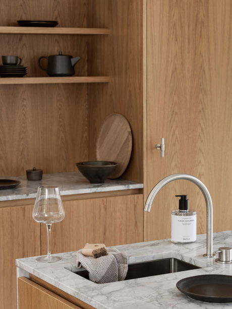 Moderne Küche mit Holzregalen, Waschbecken und eleganten Accessoires auf Marmoroberfläche.