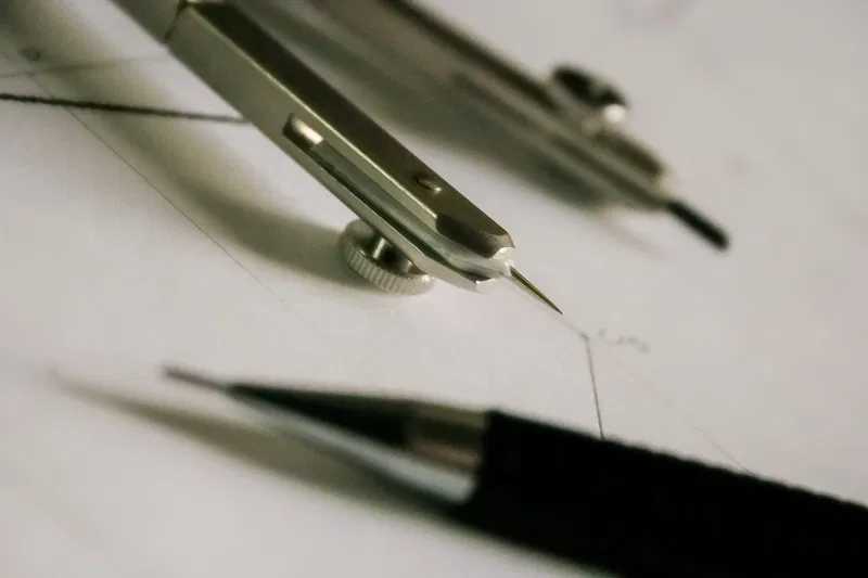 Precision drawing tools including a compass and mechanical pencil on a drafting surface.